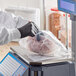 A person wearing gloves and holding a plastic bag of meat weighing it on a digital scale.