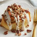 A plate with a cinnamon roll topped with white icing and pecans.