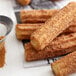 A group of churros with cinnamon sugar on top and a sieve with brown powder.
