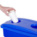 A hand putting a white cup in a blue rectangular recycling bin with a white lid.