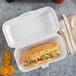A sandwich in a white foam container with chips.