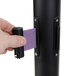 A person using an Aarco black crowd control stanchion with dual purple belts.