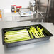 A black Cambro food pan filled with celery on a kitchen counter.