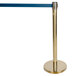 A gold metal crowd control stanchion with a blue retractable belt.
