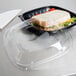 A Dart clear plastic container lid on a table with a sandwich inside.