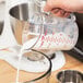 A hand pouring milk into a Cambro clear polycarbonate measuring cup.