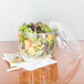 A salad in a Dart clear plastic bowl with a fork and knife on a napkin.