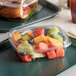 A Dart ClearPac plastic container of fruit on a tray with a sandwich and carrot.