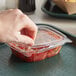 A hand holding a Dart ClearPac plastic container of salsa with a flat lid.