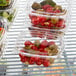 A shelf with Dart ClearPac plastic containers filled with tomatoes, olives, and salad.
