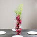 A clear square acrylic vase with red flowers and a green leaf on a table.