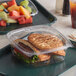 A Dart ClearPac plastic container with a sandwich and fruit in it on a table.