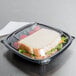 A sandwich in a Dart black square plastic bowl with a clear lid.