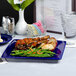 A Tuxton cobalt blue square china plate with a plate of food and a glass of water on a table.
