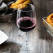 A Thunder Group plastic wine glass filled with red wine next to a basket of onion rings.