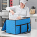 A woman in a grey visor opening a blue Choice insulated food delivery bag to reveal a plastic container inside.