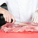A person using a Victorinox Cimeter Knife to cut meat on a table.