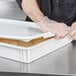A person wearing gloves puts a lid on a white Cambro pizza dough proofing box.