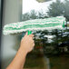 A hand using a Unger Monsoon Plus green and white window cleaner with a plastic T-bar.