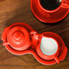 A red Fiesta creamer and pitcher on a table with a red coffee cup and saucer.