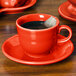 A red Fiesta saucer with a cup of tea and a bag in it.
