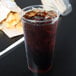 A Solo Ultra Clear plastic cup filled with soda and ice on a table with a bag of chips.