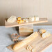 An American Metalcraft olive wood serving board with cheese and bread on a table.