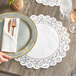 A hand holding a plate with a Normandy lace doily, napkin, and fork on a table.