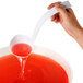 A hand holding a white Fineline disposable ladle pouring red liquid into a bowl.