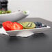A white porcelain sauce dish with a kiwi, strawberries, and blueberries.
