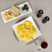 A white square porcelain coupe bowl filled with scrambled eggs and a plate of toast.