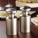 Two American Metalcraft stainless steel tall shakers with fine holes on a table.