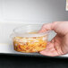 A hand holding a Solo MicroGourmet plastic deli container of food.