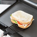 A sandwich on a black spatula being cut on a grill.