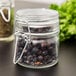 An American Metalcraft miniature glass hinged apothecary jar filled with black pepper and herbs.