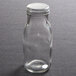 A clear glass American Metalcraft milk bottle with a round PET cover on a table.