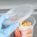 A hand in a blue glove holding a Solo clear plastic container of food.