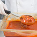 A person using a Vollrath Jacob's Pride black solid oval Spoodle to serve meatballs in sauce.