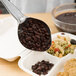 A Vollrath black perforated oval spoodle spoon serving beans and pasta.