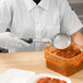 A person in white gloves using a Vollrath black perforated round Spoodle to remove food from a container.
