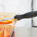 A black Vollrath Spoodle in a glass container of food with a knife handle.