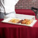 A chef using a Cambro Clear Dome Display Cover to cover a tray of pastries on a white table with a red tablecloth.
