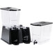 Two Carlisle black plastic beverage dispensers with clear containers and black lids.