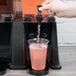 A hand pouring pink liquid into a Carlisle plastic beverage dispenser.