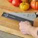 A hand uses a Mercer Culinary knife to cut a yellow tomato on a table.