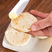 A person using a Fineline white plastic sandwich spreader to butter a biscuit.