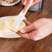 A person using a Fineline white plastic sandwich spreader to spread butter on a piece of bread.