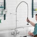 A man using a Regency wall mount pre-rinse faucet to fill a glass with water.