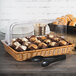 A Polycarbonate cover on a basket of muffins and pastries on a table.