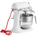 A white KitchenAid countertop mixer with standard accessories, including a wire whip, and a bowl.